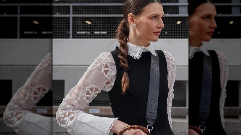 woman white lace shirt black sweater vest ponytail