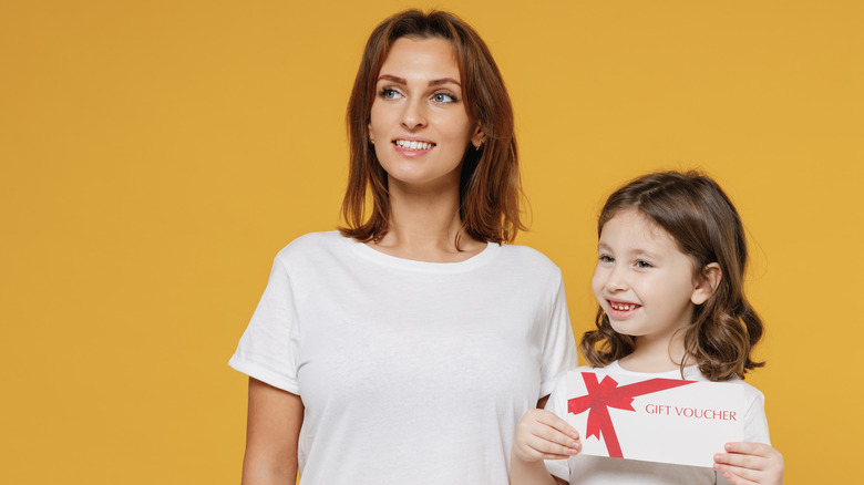 woman with daughter holding "gift voucher" coupon; orange background