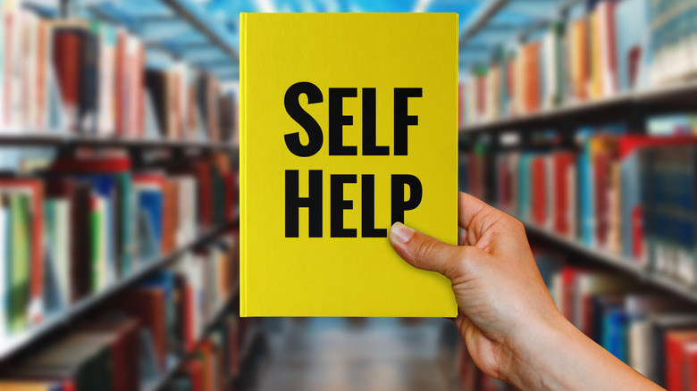 hand holding up yellow "Self help" book in library