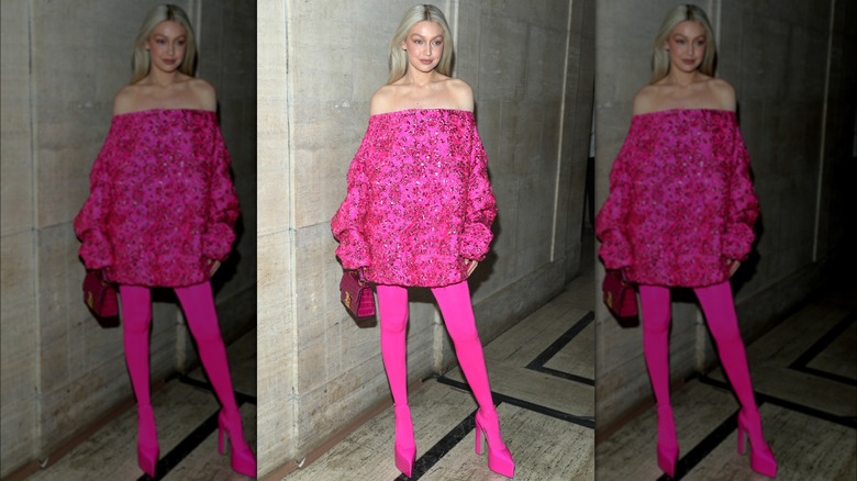 Gigi Hadid wearing a bright pink dress, off the shoulder, long sleeves, no shape, accompanied by pink tights and shoes.