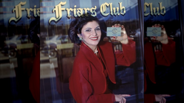 Gloria Allred under Friars Club sign holding membership card