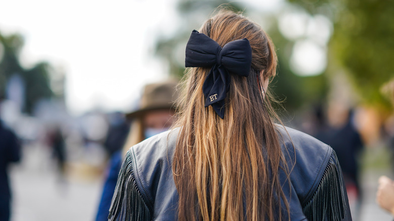 person wearing a hair bow and a black leather fringed jacket during Paris Fashion Week 