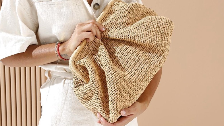 Model holding an oversized natural fiber clutch