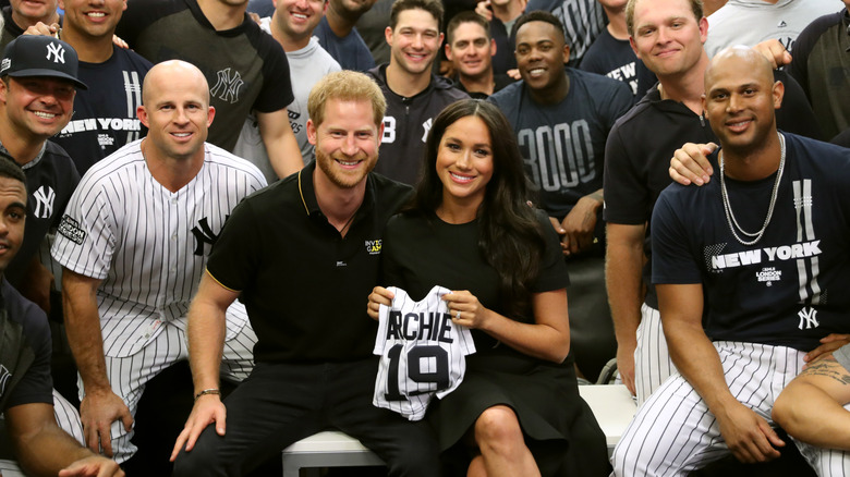 Meghan Markle and Prince Harry pose with baby onesie and baseball team