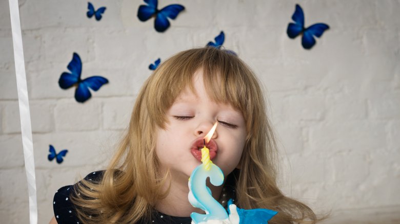 young girl blue butterflied blowing out birthday candle