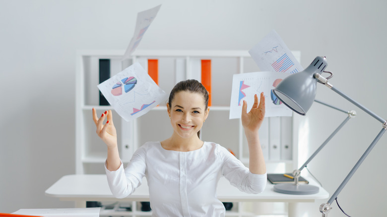 woman smiling and throwing papers in air at work