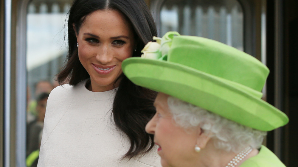 Meghan Markle smiles at the Queen who is wearing a green hat