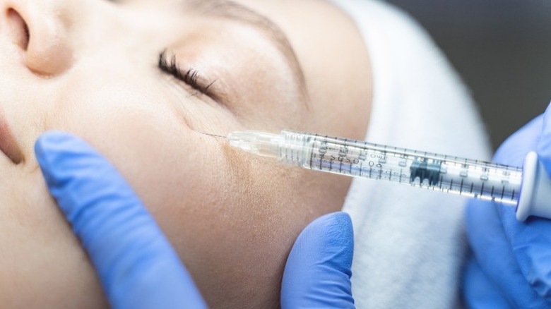 Woman's face alongside needle for under eye filler injection