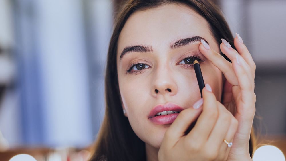 Woman applying eye makeup in the mirror