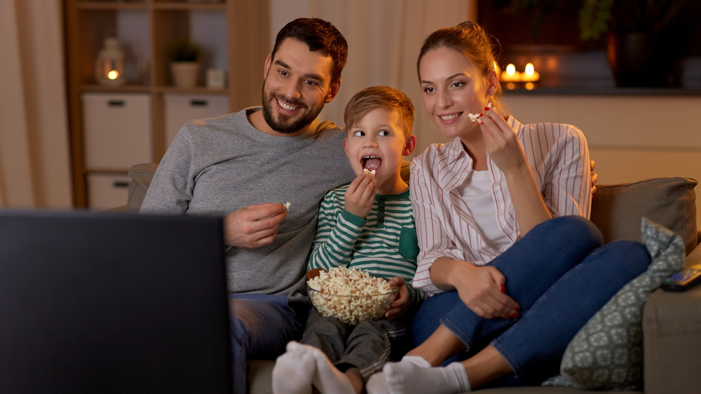 Father, son, and mother watching television while eating popcorn