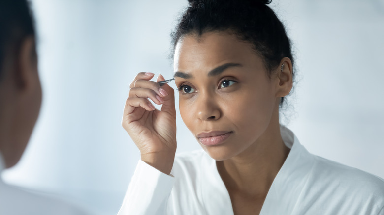 woman plucking eyebrow in mirror