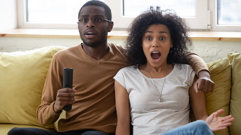 Couple watching TV looking surprised