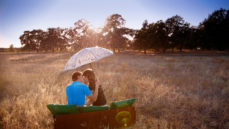 couple sitting in field kissing under umbrella 