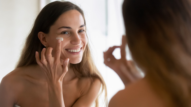 woman applying moisturizer in mirror