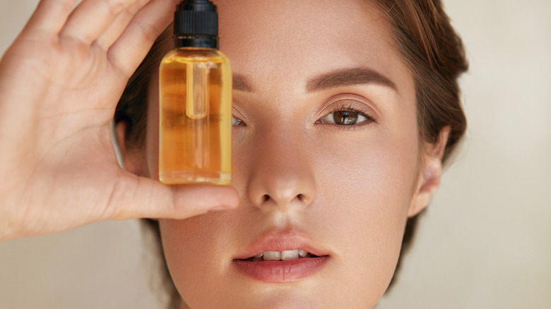 A woman holding a bottle of oil over her face.