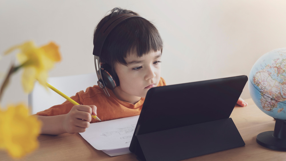 Child drawing while wearing headphones and looking at a tablet 