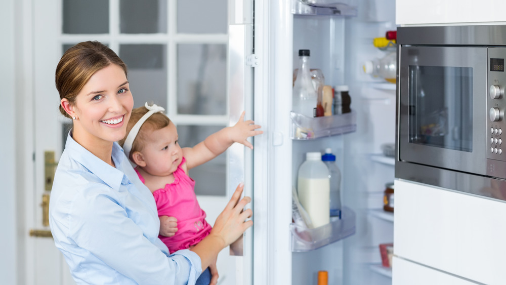 A smiling woman and baby opening a fridge 