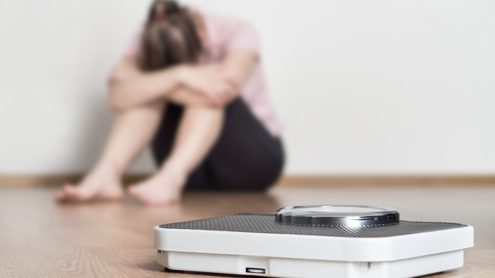 Woman struggling and out of focus behind scale