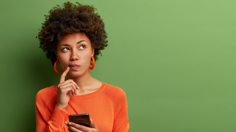 woman thinking with phone in hand