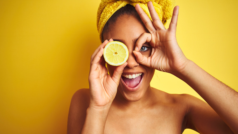 Woman holding a lemon wedge over her eye with a yellow background 