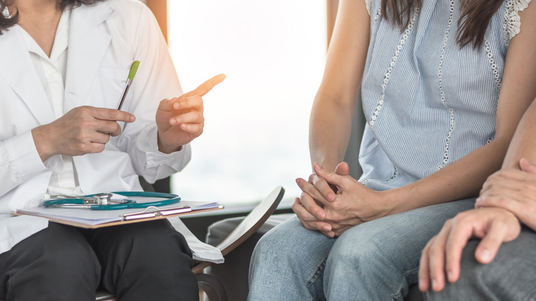 doctor with clipboard talking to man and woman