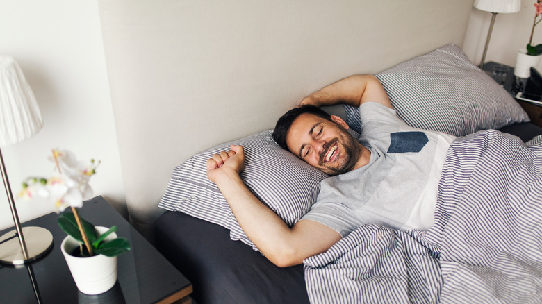 person waking up in bed, while stretching and smiling