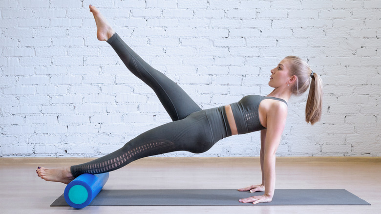 Woman wearing gray balancing on a foam roller with her toe pointed