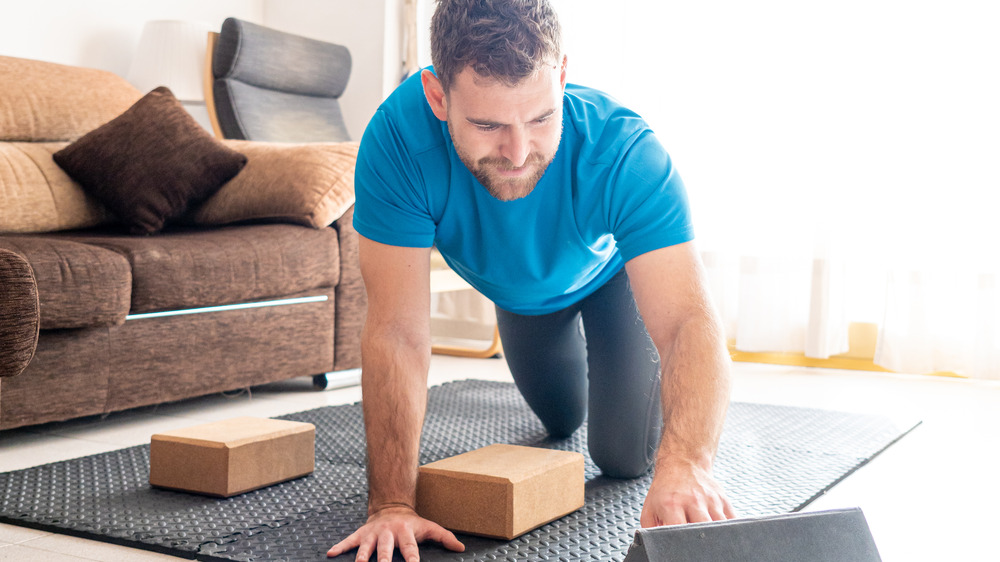 Man preparing for yoga on tablet in living room. 