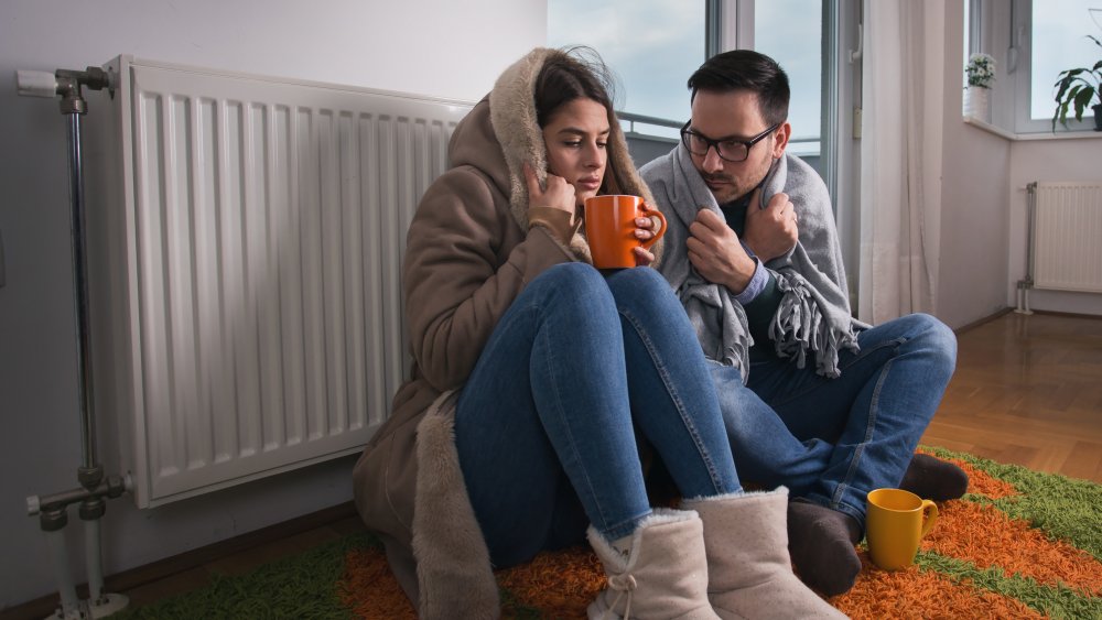 Two people huddling close together and shivering under blankets