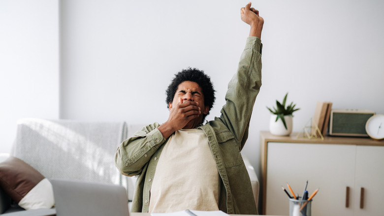 Man yawning and stretching at his laptop