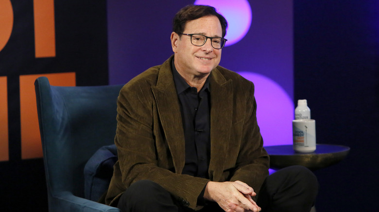 Bob Saget wearing a brown jacket and speaking in an interview