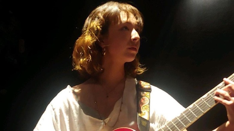 Aubrey Anderson-Emmons in a white t-shirt, playing guitar