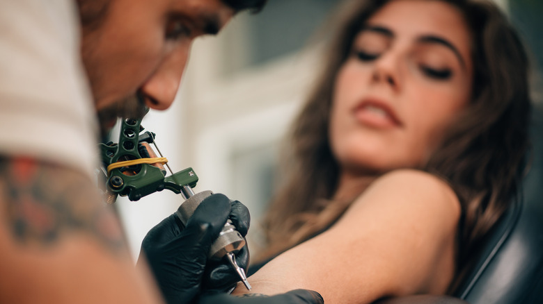 Tattoo artist creating tattoo on woman's arm with focus on the equipment