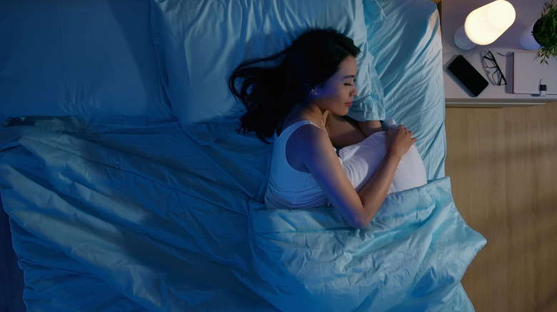 woman sleeping in dark room under blue sheets