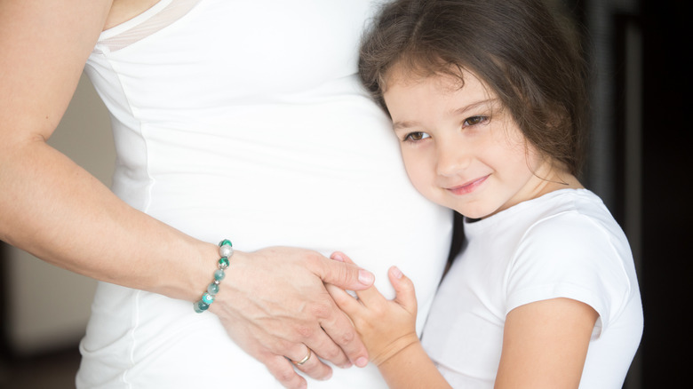 Girl listening to mother's pregnant stomach