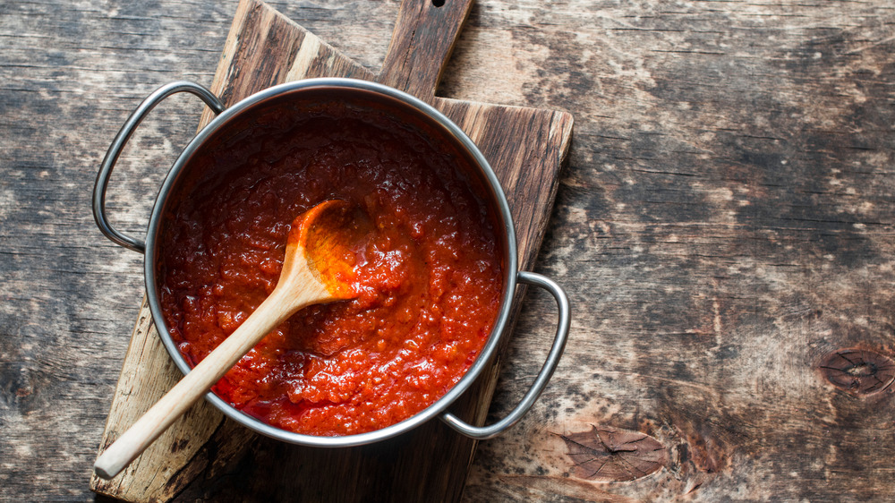 A pot of red sauce on a cutting board