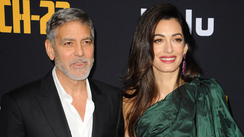 Amal Clooney smiling with her arm around George Clooney at an event