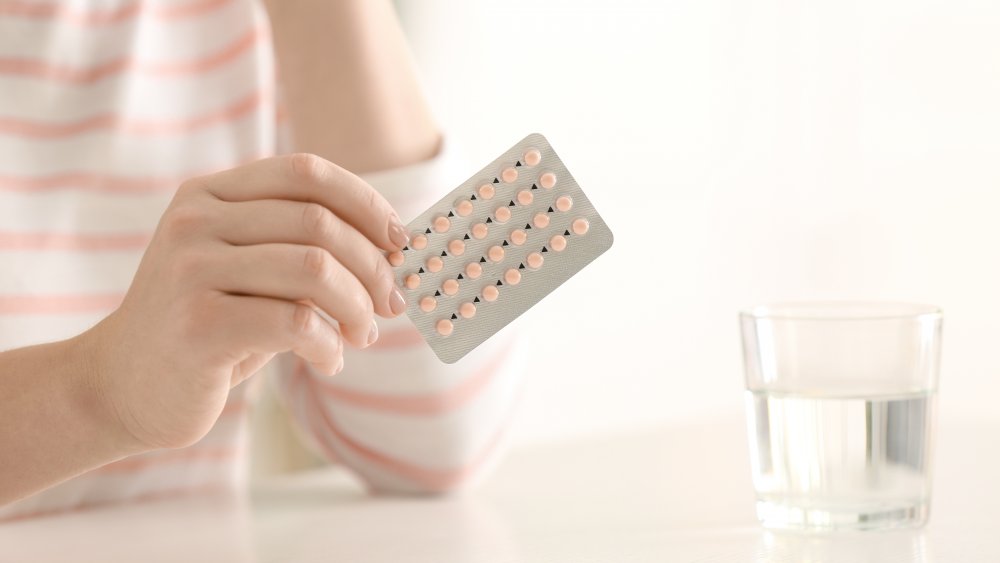 woman holding contraceptive pills at a table with a glass of water