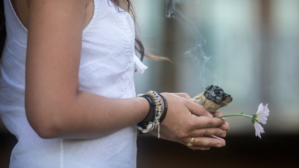 A woman holding a flower and a smudge stick 