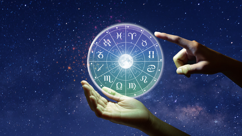 Two hands holding the zodiac wheel in the night sky 