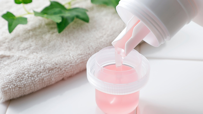 Person measuring pink laundry detergent into a measuring cup.