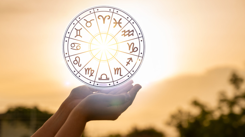 Zodiac wheel held by hands in front of the sky