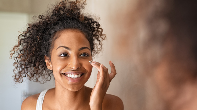 smiling Black woman applying lotion to face in mirror