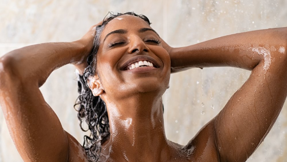 a Black woman washing her hair in a large luxury shower