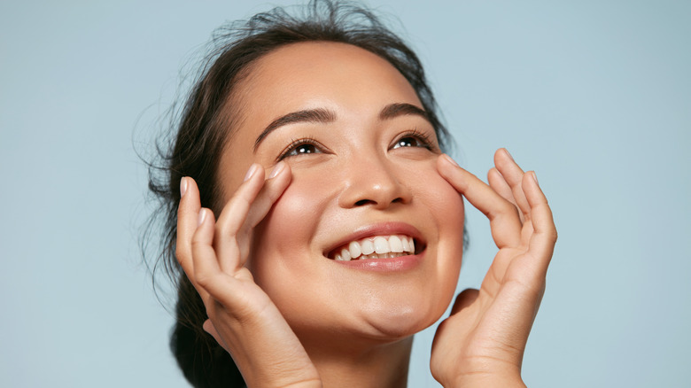 A woman smiling and touching her face 