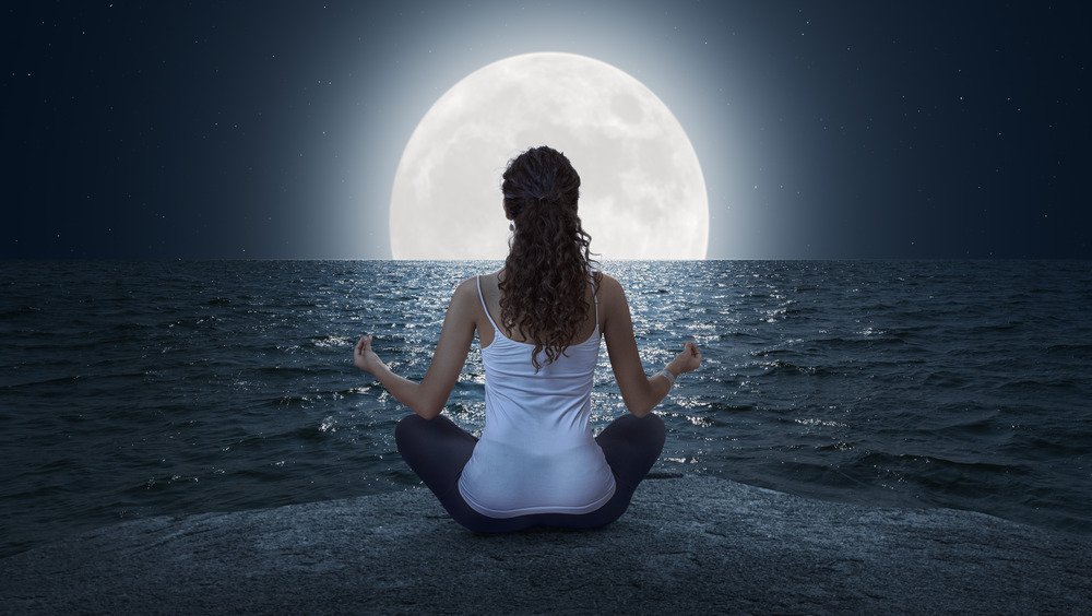 Woman meditating under full moon.