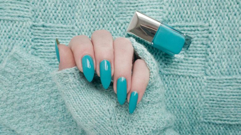 Blue almond-shaped nails with nail polish bottle