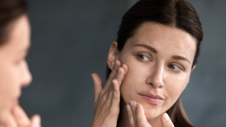 Woman with dark hair looking in the mirror at her face for signs of scarring from electrolysis