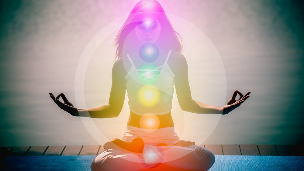 A seated person with chakras illuminated by colors 