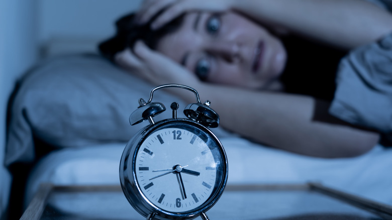 Woman looking anxiously at alarm clock